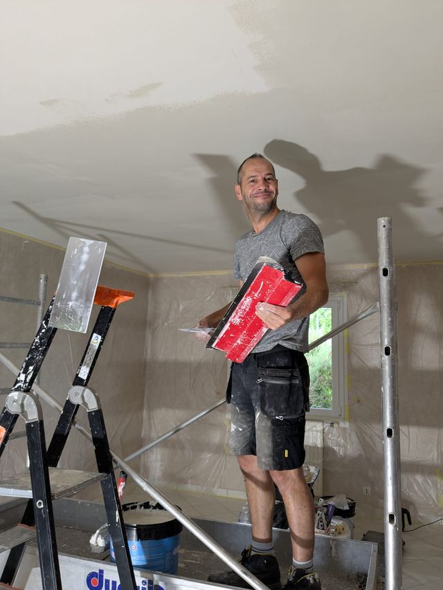Christophe Léauté sur un échafaudage, lisseuse en main, pendant l'enduit d'un plafond