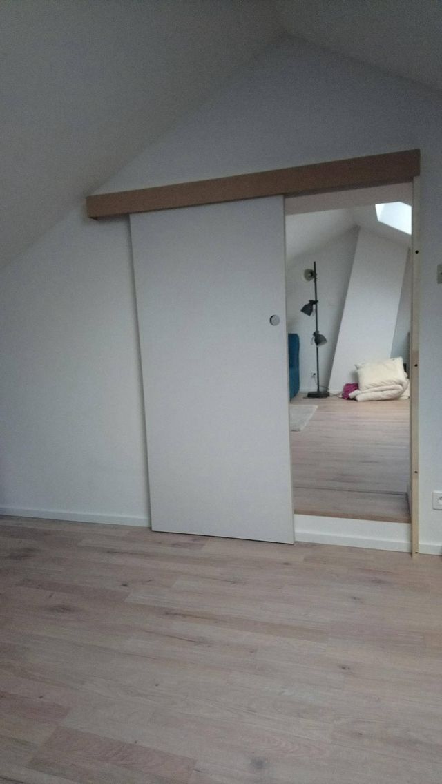 Porte coulissante blanche sous rampant dans une chambre mansardée