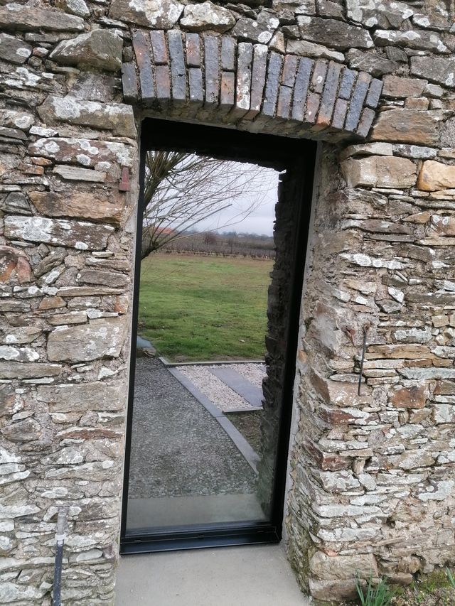 Porte-fenêtre aluminium noir à grand vitrage ouvrant sur le jardin, dans une ouverture en pierre